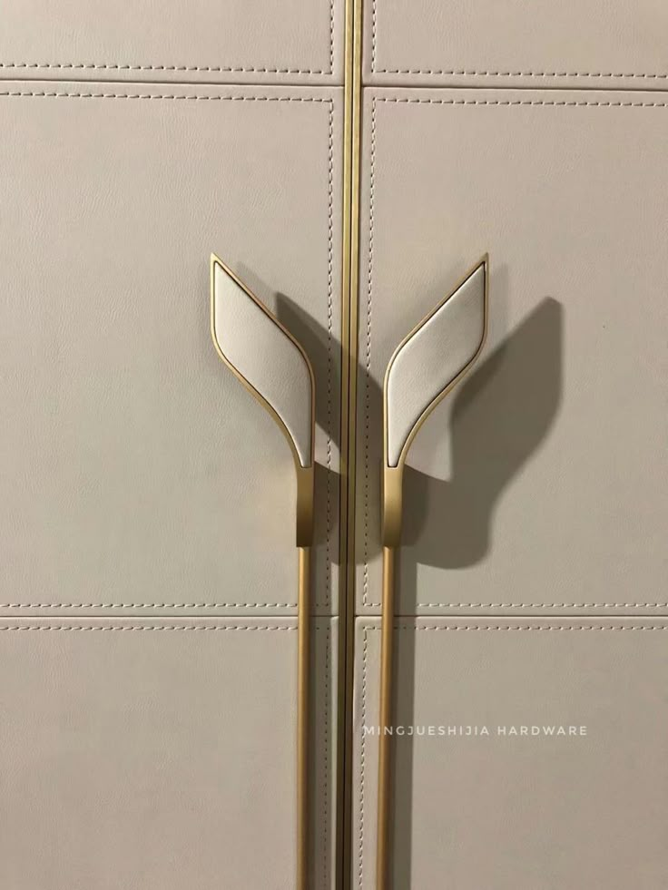 two gold handles on the side of a beige door with white leather panels and metal bars