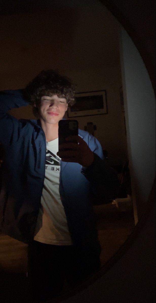 a young man taking a selfie with his cell phone in the dark while wearing a blue jacket