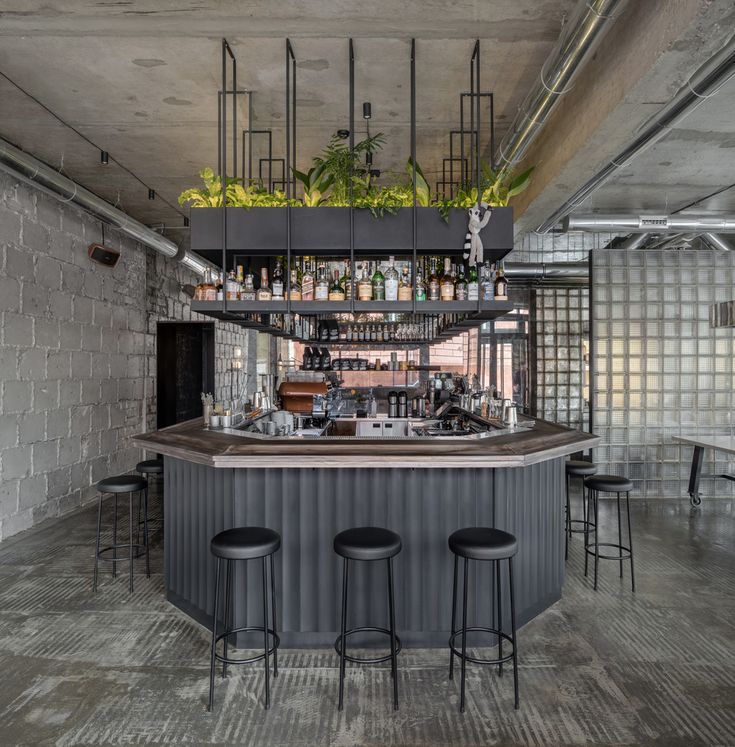 a bar with stools and plants hanging from the ceiling in an industrial style restaurant