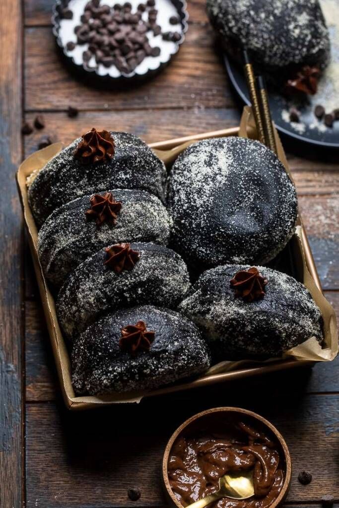 chocolate donuts with powdered sugar on top in a wooden box next to other desserts