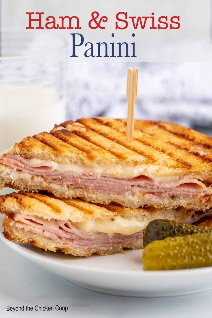 ham and swiss panini on a white plate with pickles next to the sandwich