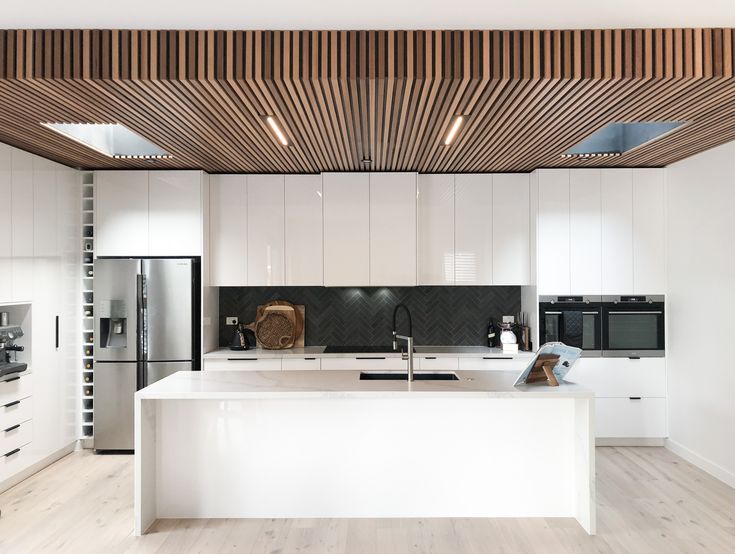 a modern kitchen with white cabinets and wood ceilinging is seen in this image from the front view