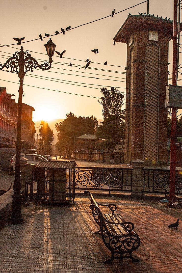 a bench sitting on the side of a road next to a clock tower at sunset