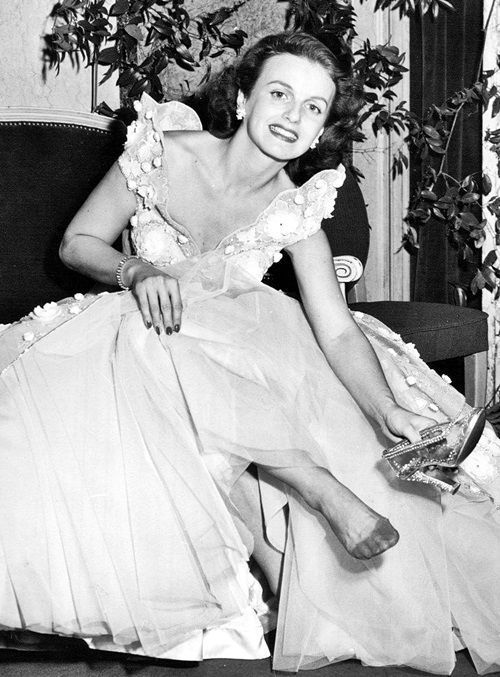 a black and white photo of a woman in a dress sitting on a chair with her legs crossed