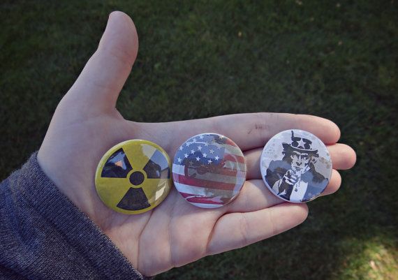 someone holding three buttons in their hand with an american flag and nuclear symbol on them