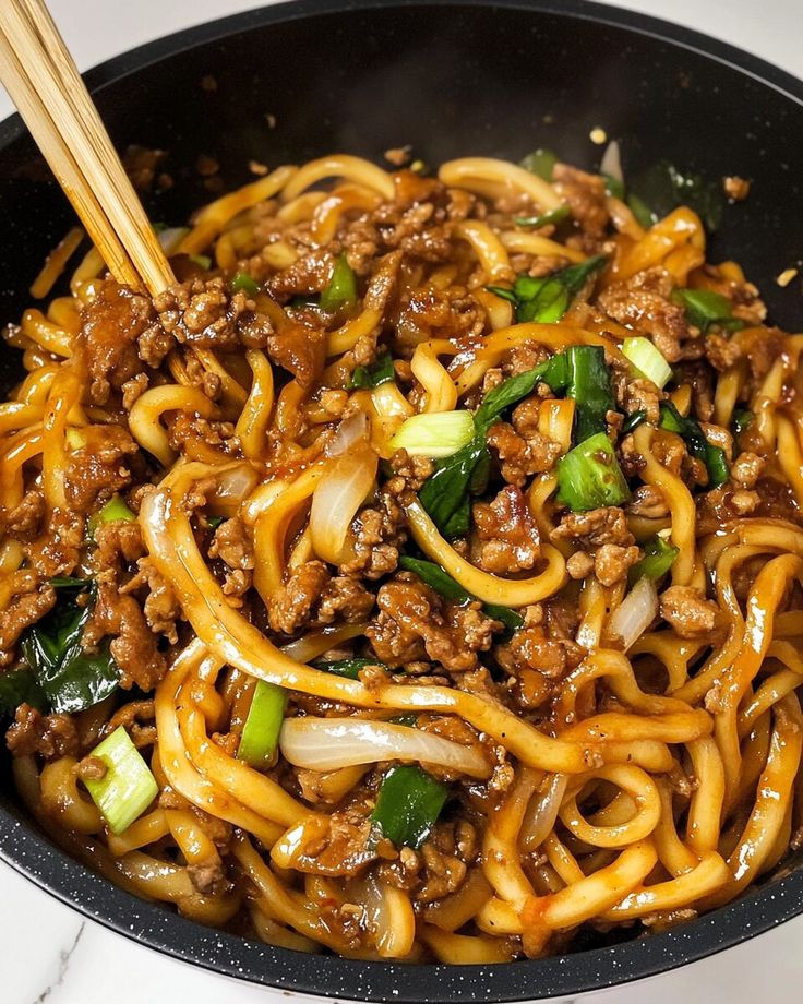 a bowl filled with noodles and meat on top of a white counter next to chopsticks