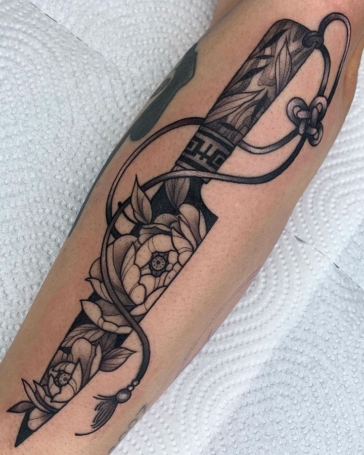 a tattoo on the leg of a woman with an arrow and flowers in it,