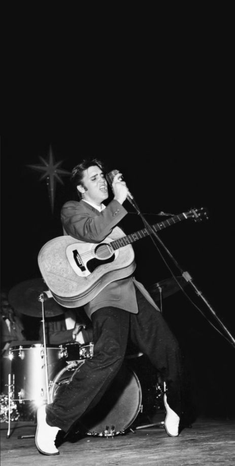 a man with a guitar standing in front of a microphone