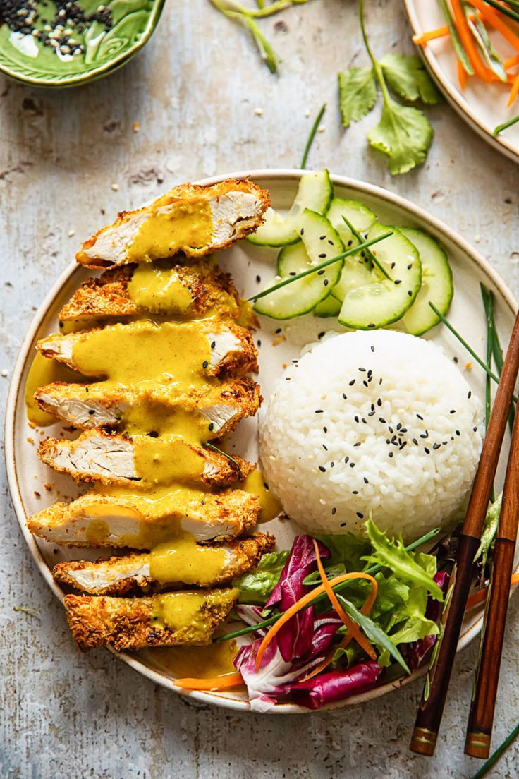 a plate with chicken, rice and vegetables on it next to chopsticks and sauce