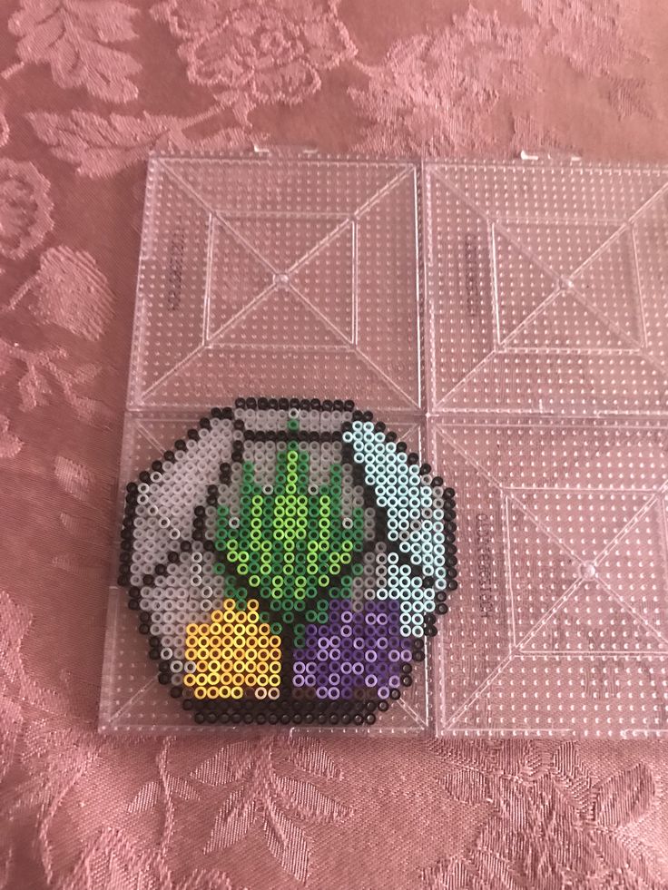 a plastic tray with a cross stitch cactus and fruit design on the side, sitting on a pink surface