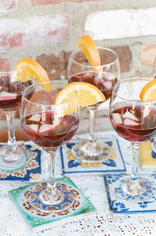 four glasses filled with red wine and orange slices on top of a blue table cloth