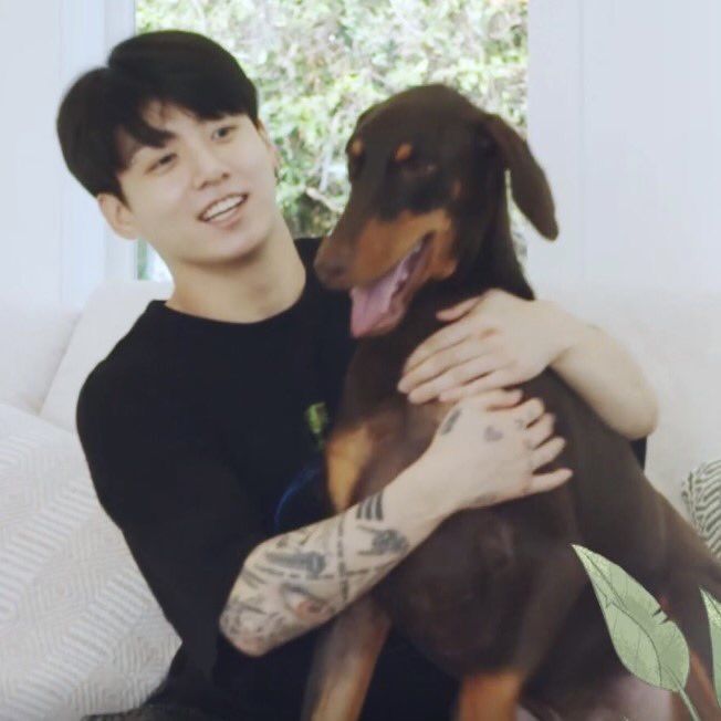 a man sitting on a couch with his arm around a dog's head and smiling