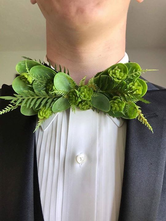 a man wearing a suit and bow tie with green plants on it's lapel