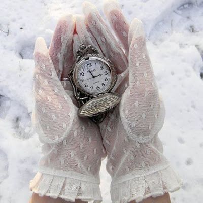 a person's hands with white gloves and a watch on them in the snow