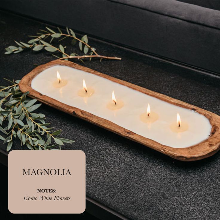 three candles in a wooden tray on a black countertop with an olive branch next to it