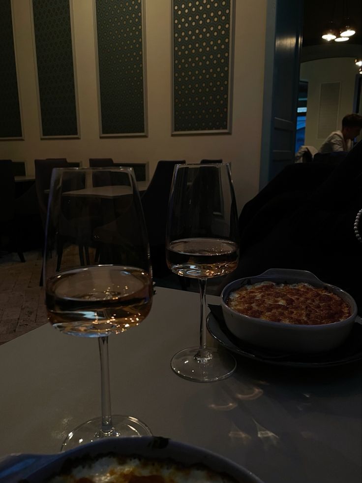 two glasses of wine sitting on top of a table next to plates and bowls of food