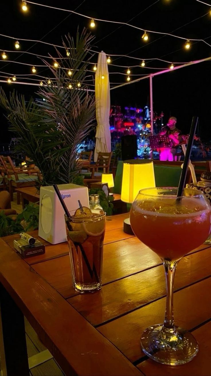 two drinks sitting on top of a wooden table next to an umbrella covered area with lights