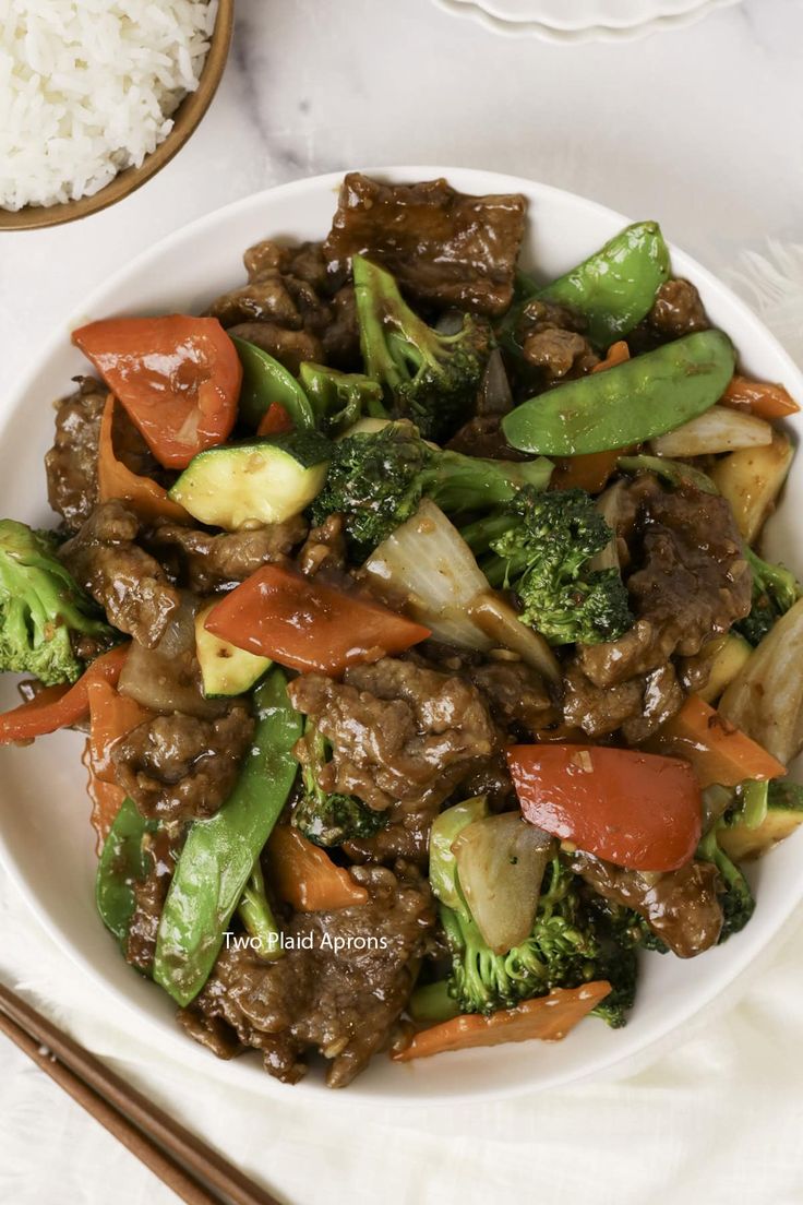 a white plate topped with beef and veggies next to rice