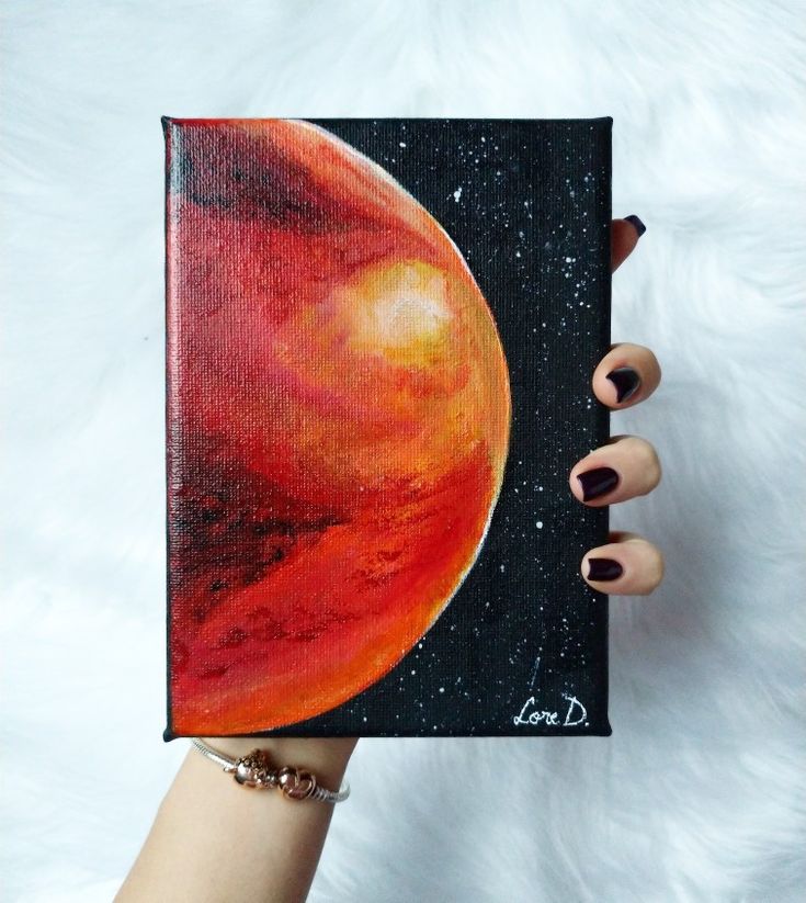 a woman's hand holding up a small book with an orange and black painting on it