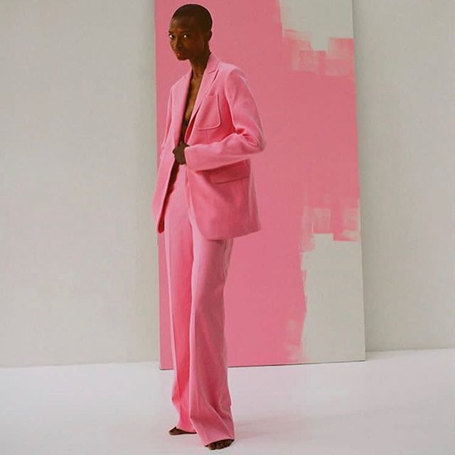 a man in a pink suit standing next to a large piece of art on the wall