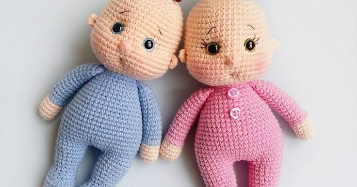 two crocheted dolls laying next to each other on a white surface, one is pink and the other is blue