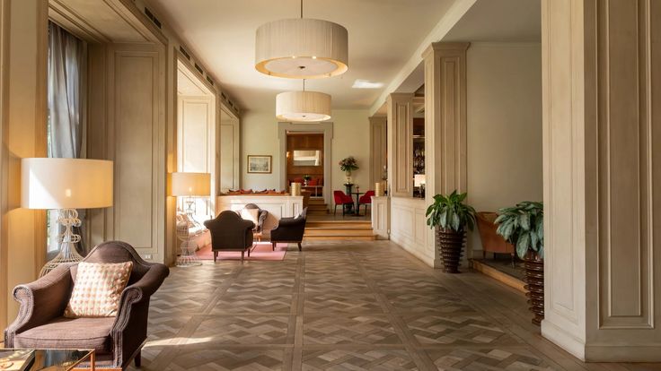 an empty hallway with chairs and lamps on either side of the hall, leading to another room