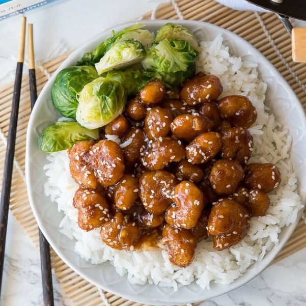 a white plate topped with meat and veggies next to chopsticks on top of rice