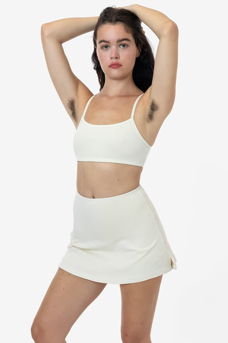 a woman in a white skirt and crop top posing for the camera with her hands on her head