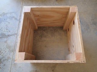 a wooden box sitting on top of a cement floor next to a piece of wood