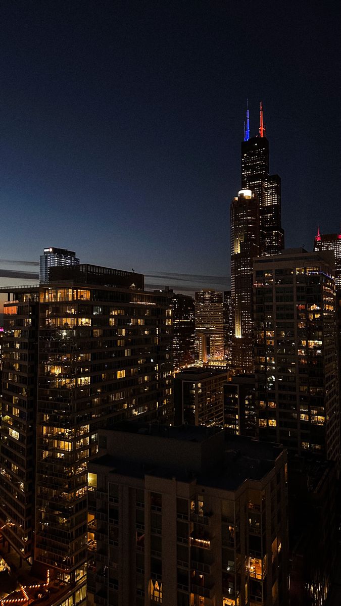 the city skyline is lit up at night with bright lights and skyscrapers in the background