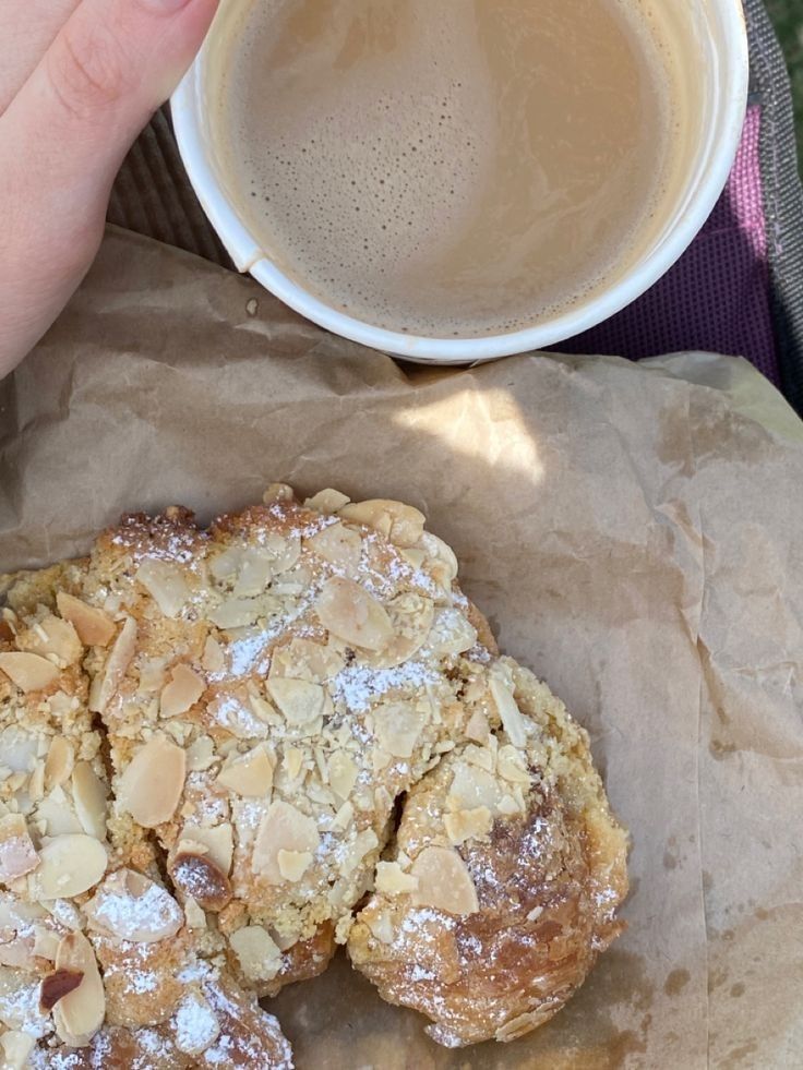 a person holding a cup of coffee and some food on top of a piece of wax paper