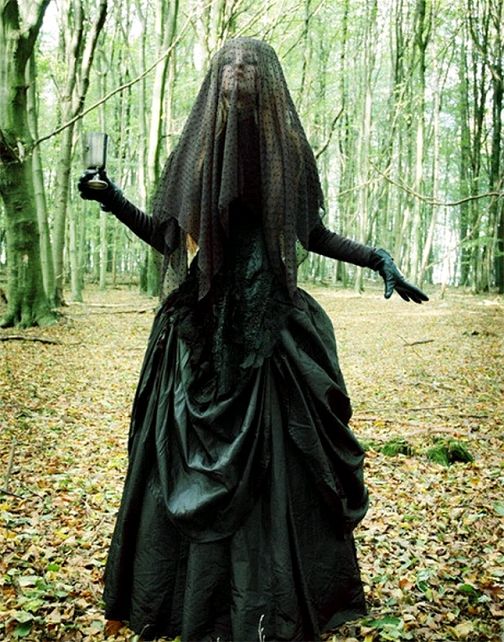 a woman dressed in black is walking through the woods with her arms spread wide open