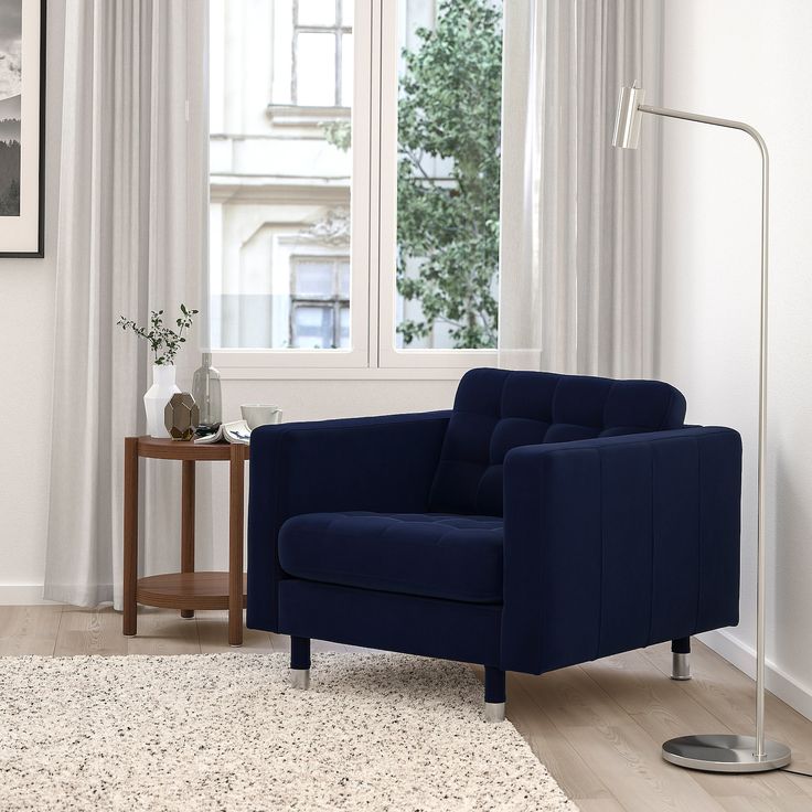 a blue chair sitting in front of a window next to a table with a vase on it