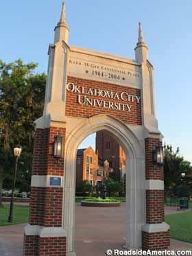 an arch in the middle of a brick and stone entrance to a college campus with trees on either side