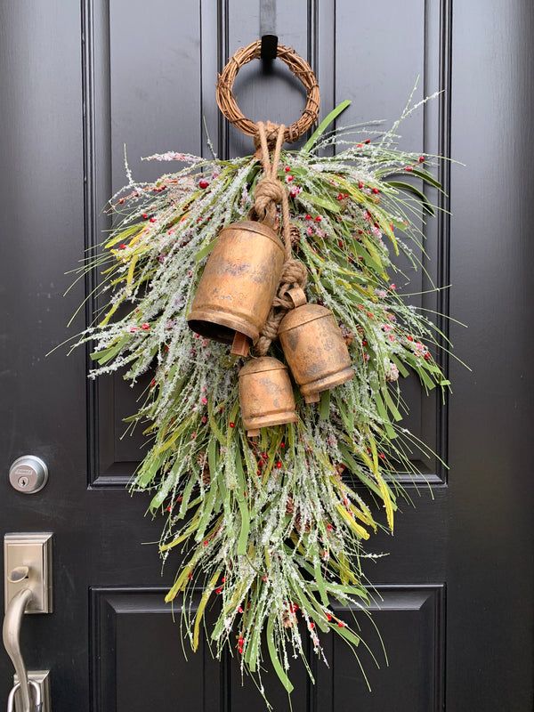 a wreath with three bells hanging from it's side on a black front door