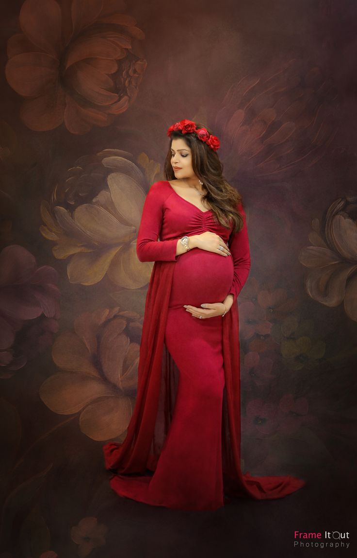 a pregnant woman wearing a red dress and flower in her hair, standing against a floral background