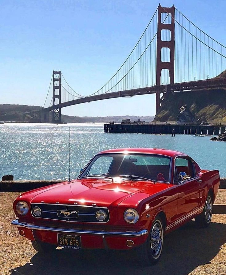 an old red car parked in front of the golden gate bridge