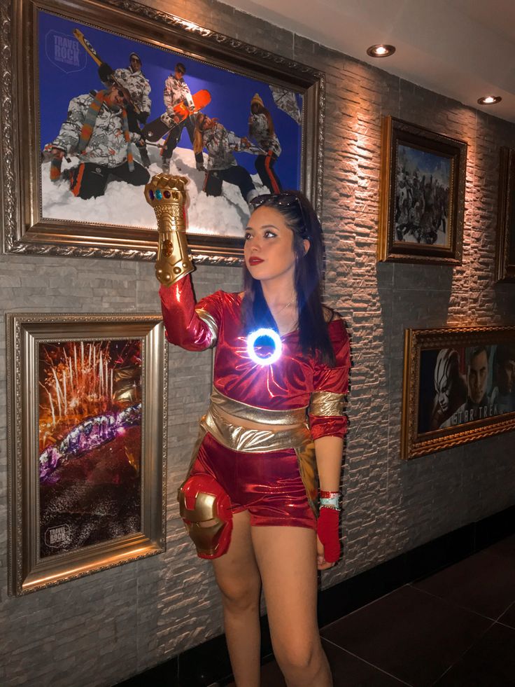 a woman dressed in costume standing next to pictures on the wall and holding a light up item