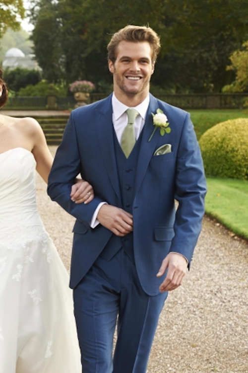 a bride and groom are walking down the path in their wedding day attire, smiling at the camera