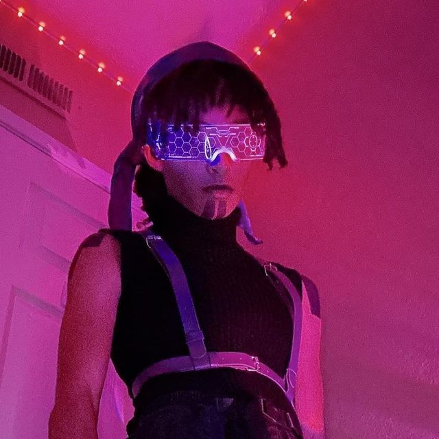 a woman wearing futuristic gadgets in a room with pink lights on the ceiling and behind her is a neon light