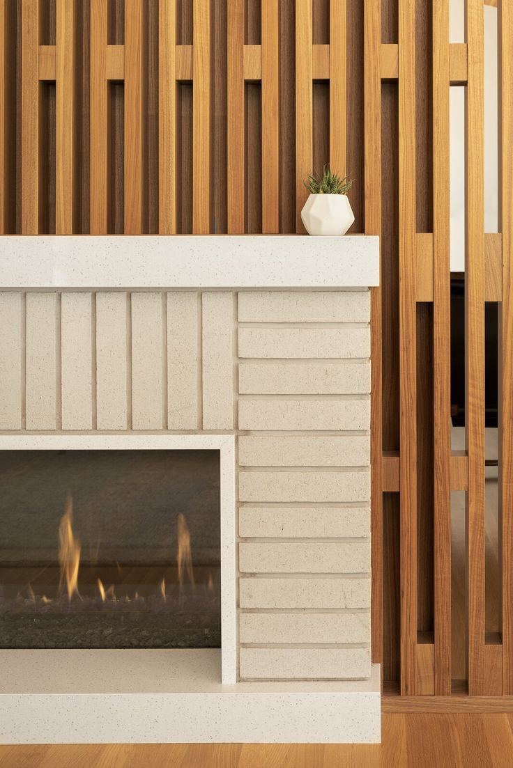 a white fireplace with wood paneling and a potted plant