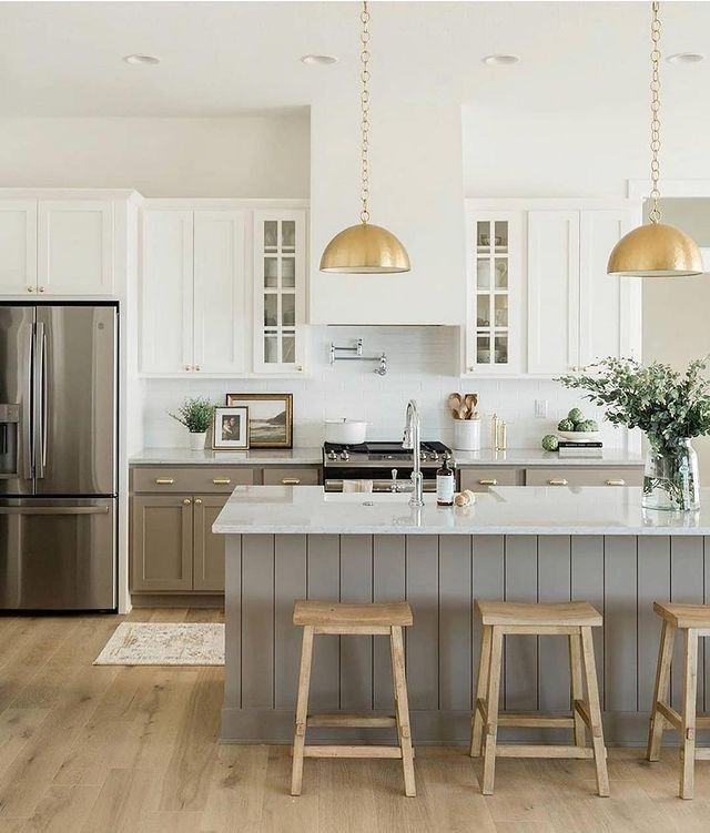 a kitchen with two stools in front of the island and gold lights hanging from the ceiling