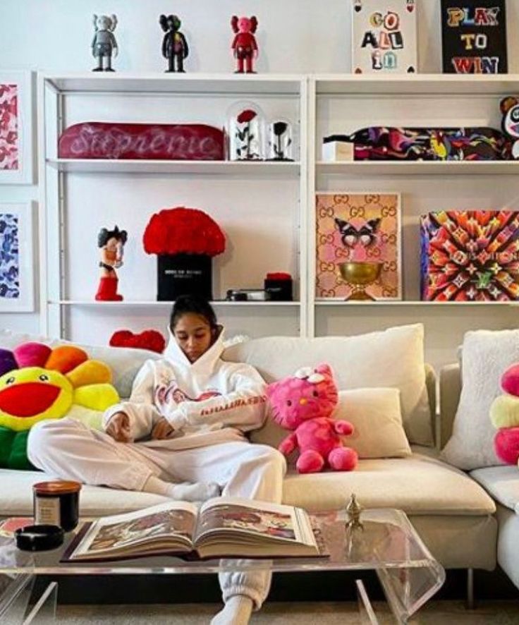 a woman sitting on top of a white couch in front of a bookshelf filled with stuffed animals