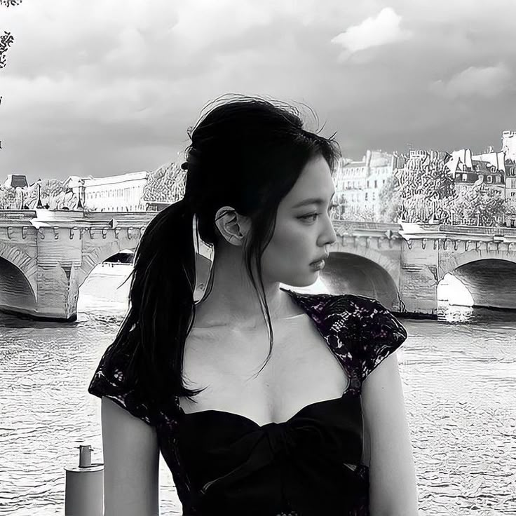 a woman standing next to a body of water with a bridge in the back ground