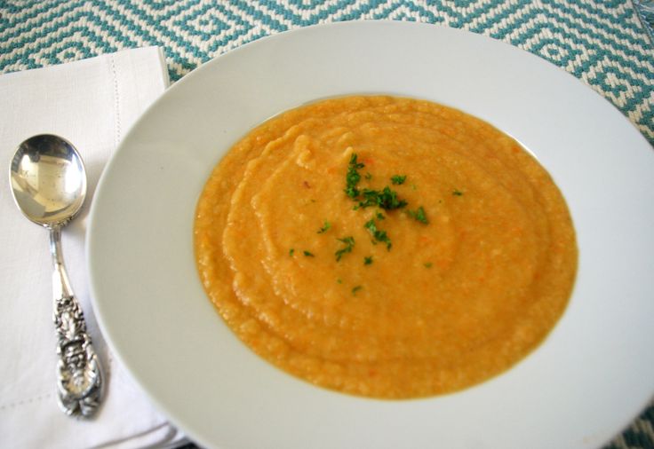 a white plate topped with soup next to a silver spoon and napkin on top of a table