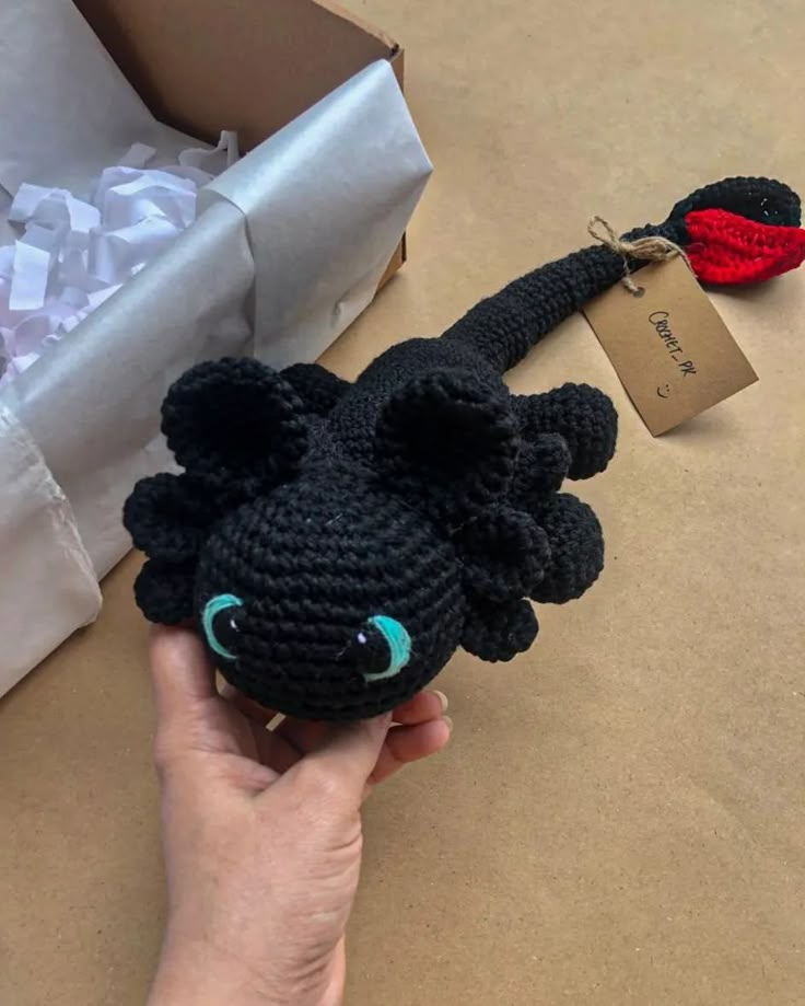 a crocheted black cat keychain with green eyes and red nose, sitting on top of a cardboard box