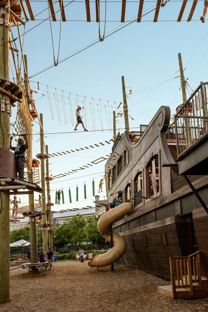 people are playing on an outdoor play area with ropes and climbing equipment in the background