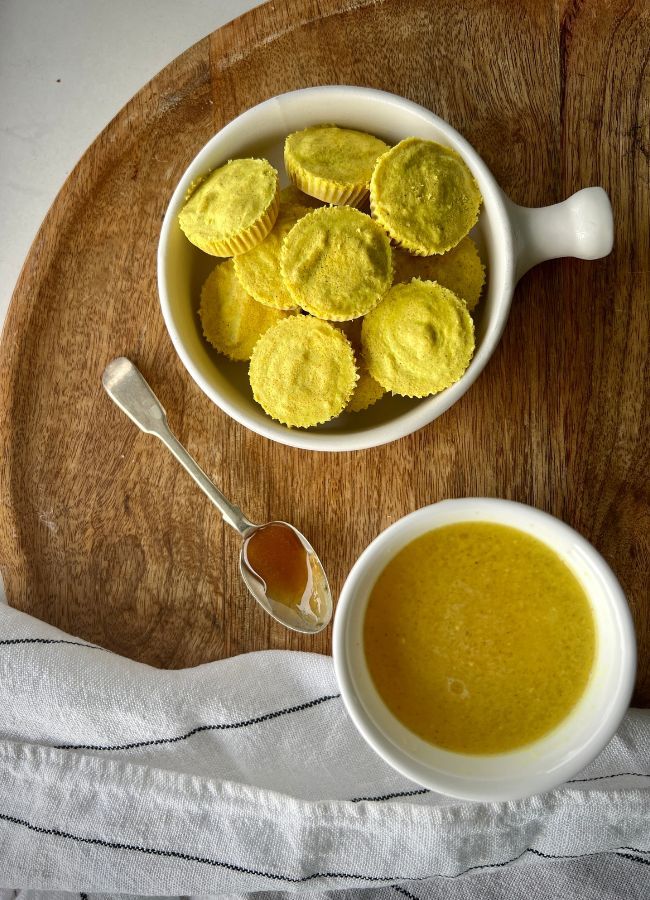 a bowl filled with yellow cookies next to a cup of soup on top of a wooden cutting board