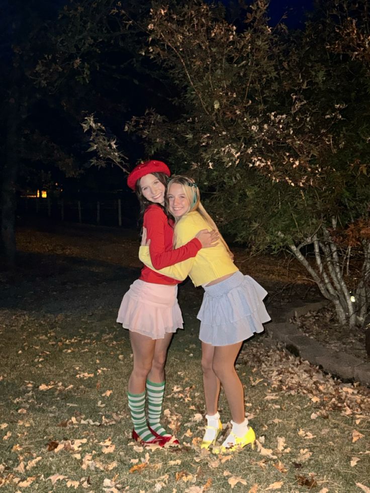 two young women hugging each other in the park at night time with leaves on the ground