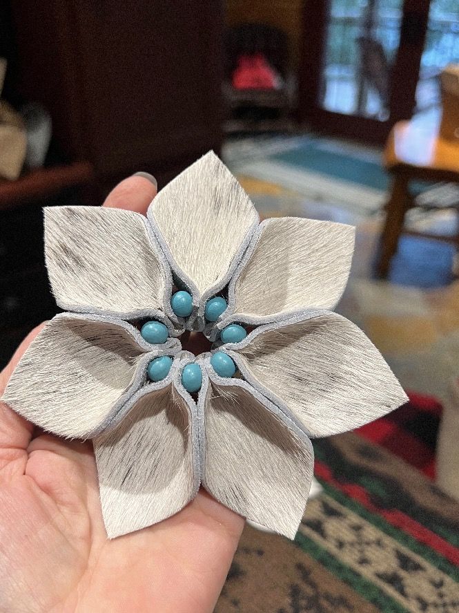 a hand holding a white and gray flower brooch with blue beads on it's center